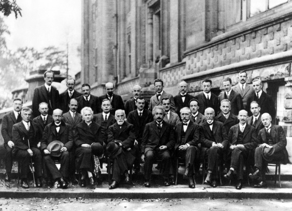 29 persone (una sola donna, Marie Curie), 17 erano o sarebbero diventati premi Nobel, per la fisica o la chimica. Sono i partecipanti alla V Conferenza Solvay, dedicata ufficialmente a elettroni e protoni, ma che in realtà ospitò il primo grande dibattito sulla fisica quantistica, mettendo a confronto i sostenitori dell’interpretazione della meccanica quantistica secondo la scuola di Copenhagen e un nutrito gruppo di scettici che non credeva nella sua natura intrinsecamente probabilistica. I primi avevano come leader indiscusso Bohr e i secondi erano rappresentati da Einstein. I due scienziati si contrapposero a colpi di esperimenti mentali (Gedankenexperimente). Sono entrate nella leggenda le animate discussioni che iniziavano già durante la colazione del mattino, quando Einstein proponeva un esperimento mentale all’attenzione di Bohr, il quale poi passava la giornata a trovare una spiegazione che rientrasse nei canoni della meccanica quantistica.